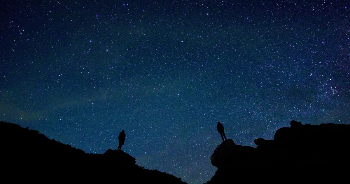 Deux silhouettes qui tentent de photographier les Perséides dans un ciel nocturne totalement noir
