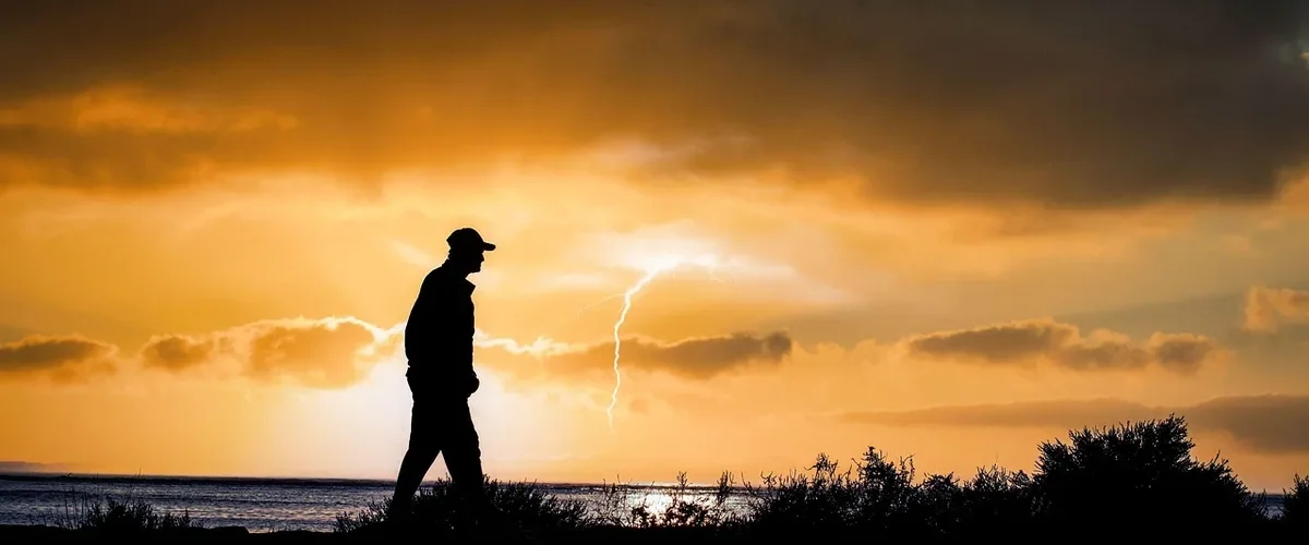 Silhouette d'un homme en marche rapide au coucher du soleil en bord de mer, entre marche et course à pied